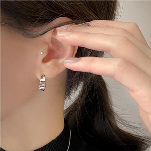 Close-up of minimalist silver hoop earrings worn on ear showing sleek metallic finish