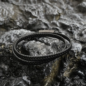 Vintage black braided leather bracelet with magnetic clasp on dark volcanic rock