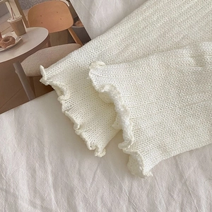 Detail of cream white knit leg warmers with ruffle edges and soft wool texture