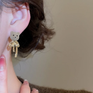 Close-up of brown flocked bear earring with gold bow knot worn by a model