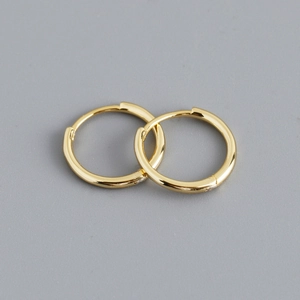 Close-up of classic golden S925 sterling silver hoop earrings on a light grey background