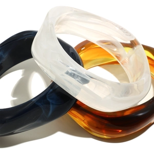 Macro shot of stylish wide twisted acrylic bangles in marble blue, cream and amber resin