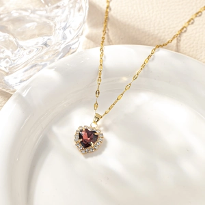 Detailed view of heart-shaped necklace with red gemstone and pavé zircon on white plate