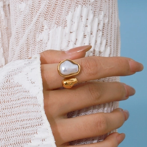 Golden stainless steel open ring featuring a white baroque pearl on a woman's hand