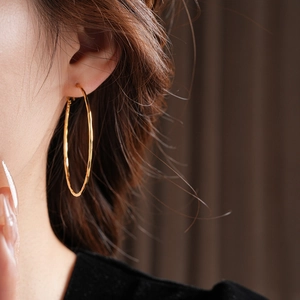 Gros plan de boucles d'oreilles créoles dorées portées sur un fond sombre élégant