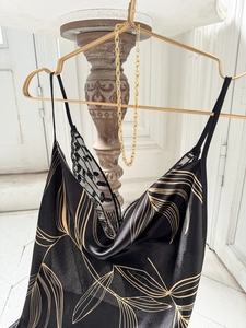 Détail d'une nuisette en satin noir avec motifs de feuilles dorées et bordure dentelle