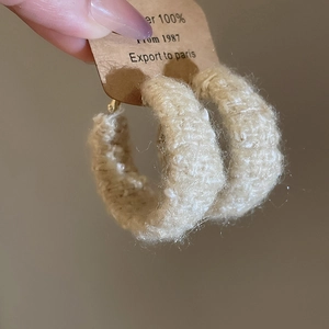 Detailansicht der beigen gestrickten runden Ohrringe mit Wollstruktur und Etikett