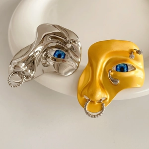 Artistic face brooch with blue eye detail and rhinestones on white ceramic bowl
