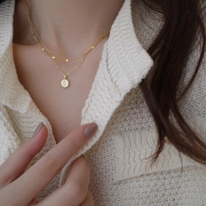 Detail of a layered gold necklace with a rose flower embossed coin pendant on a model