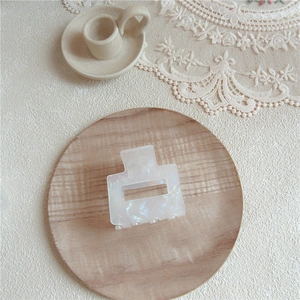 Close-up of a square acetate hair claw with iridescent pearl finish on a wooden tray