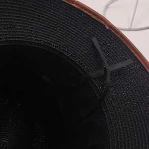 Detail of woven straw hat interior with black glitter finish and brown piping edge
