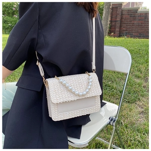 Detail of straw woven crossbody bag with pearl handle and adjustable leather shoulder strap