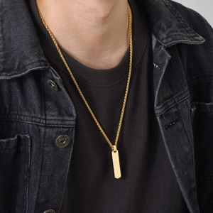 Close-up of a gold rectangular bar pendant necklace worn by a model in casual attire