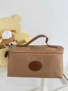Close-up of brown nylon toiletry bag with leather logo patch and metal zipper details