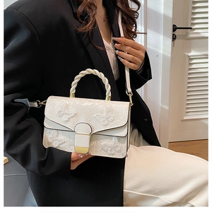 Detail of white handbag featuring delicate butterfly embroidery and woven top handle strap