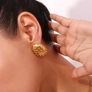 Detail view of oval 18K gold plated stainless steel textured hedgehog earrings worn on ear