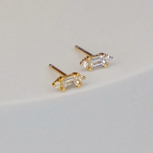 Macro detail of gold stud earrings featuring emerald cut and round cubic zirconia stones
