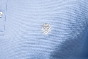 Gros plan d'un polo en coton piqué bleu clair avec broderie de blason de lion fine