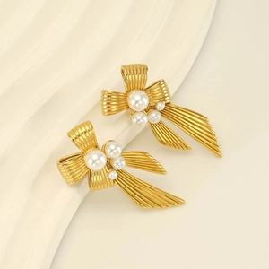 Close-up of golden bow-shaped pearl earrings with delicate textured ribbon details