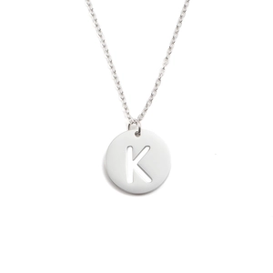 Détail macro du collier en acier argenté avec pendentif circulaire lettre K ajourée