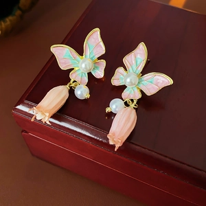 Dettaglio macro di orecchini vintage a farfalla in smalto con fiori rosa e perle su legno