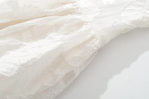 Detailed macro view of white V-neck dress featuring delicate leaf embroidery and textures