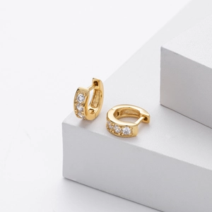 Detailed close-up of gold hoop earrings with white zircon on minimalist stone steps