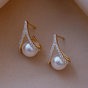 Detail of elegant gold crossover pearl earrings with sparkling white cubic zirconia