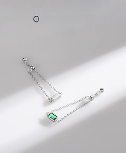 Detail of silver drop earrings featuring emerald-cut green stones and sleek chain tassels