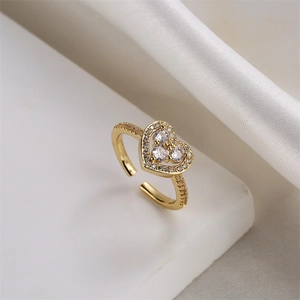 Dettaglio macro dell'anello cuore in zircone dorato su marmo bianco e seta morbida