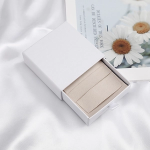 Minimalist white drawer jewelry box with soft beige velvet liner on elegant silk background