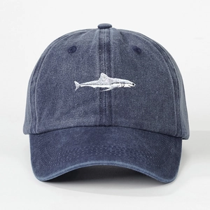 Detailed close-up of white shark embroidery on navy washed denim cotton baseball cap