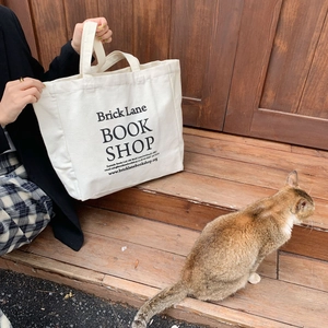 Lifestyle shot of a white canvas tote bag with black print held near a cat on wooden steps