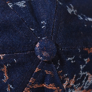 Macro detail of denim baseball cap crown showing texture and orange embroidery