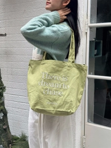Detail of light green canvas tote bag with white embroidery 'There is dream to chase' text