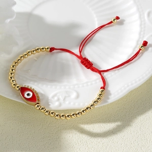 Detail of red braided Evil Eye bracelet with 4mm gold beads on white shell tray