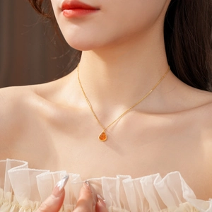Close-up of a gold-plated necklace featuring a vibrant amber teardrop pendant on the collarbone