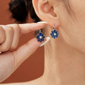 Detail of silver flower earrings with blue pear-cut petals and central crystal on ear