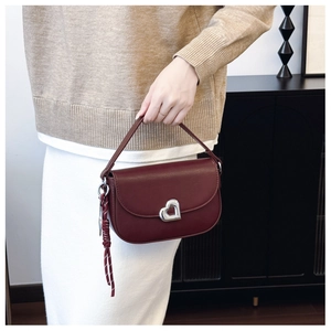 Detail of burgundy leather saddle bag with silver heart buckle and braided tassel