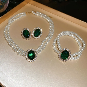 Close-up of vintage jewelry set with emerald green stones and pearls on golden tray