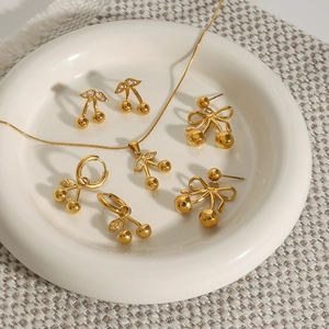 Close-up of golden cherry jewelry set with bow and white rhinestones in a ceramic dish