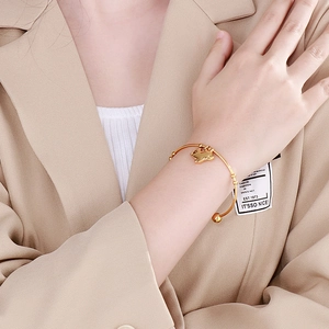 Détail d'un bracelet en titane doré avec pendentif lapin mat porté sur un blazer beige