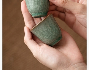 Close-up of hands holding two green Ru kiln ceramic teacups with ice crackle glaze detail