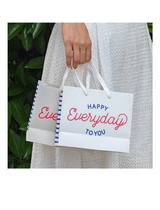 Detail of grey square gift bag with blue stripes and white silk ribbon handles