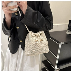 Detail of off-white straw bucket bag with green floral embroidery and rope straps