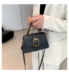Detail of black trapezoid bag with gold oval buckle and textured metallic finish