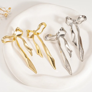 Boucles d'oreilles nœuds métalliques dorées et argentées sur un plateau en céramique