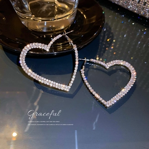 Boucles d'oreilles créoles cœur argentées ornées de strass brillants sur fond de miroir