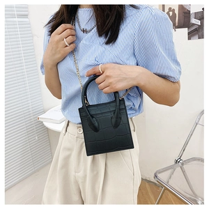 Detail of black crocodile pattern mini handbag with gold chain strap and dual handles
