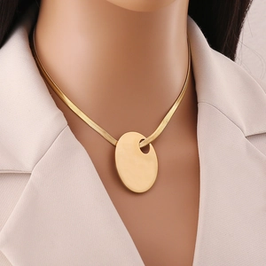 Golden snake chain necklace with smooth oval hollow pendant worn by a model in a beige suit